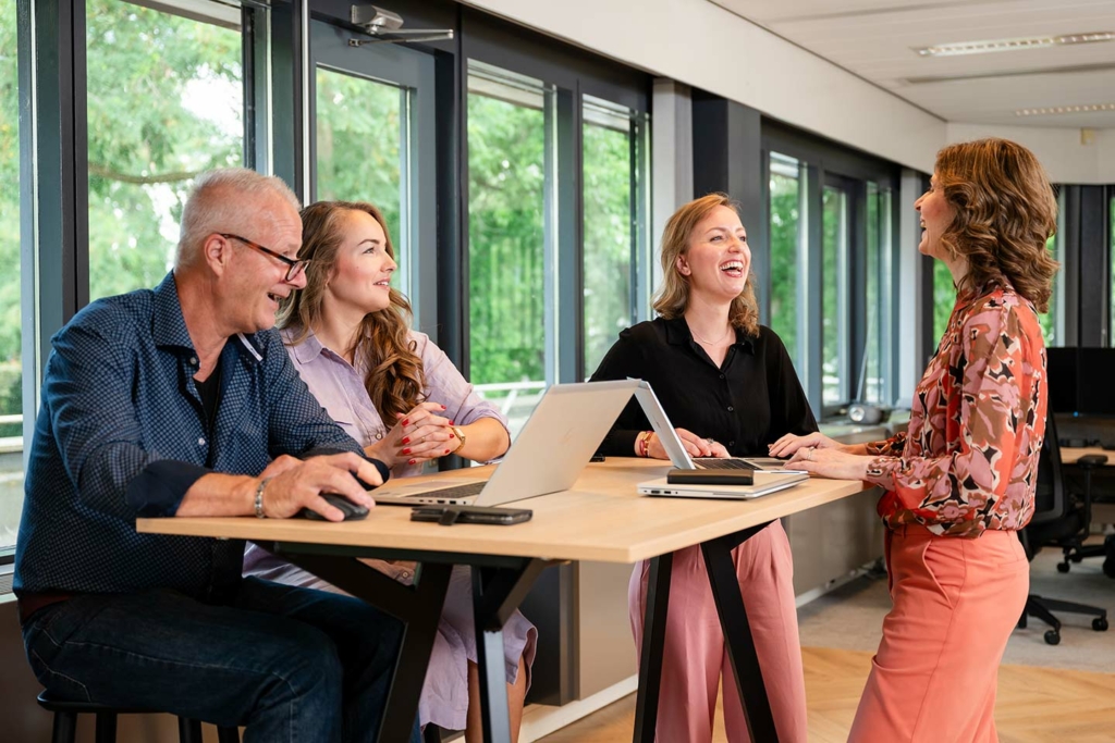 Vier lachende medewerkers in een informeel werkoverleg.