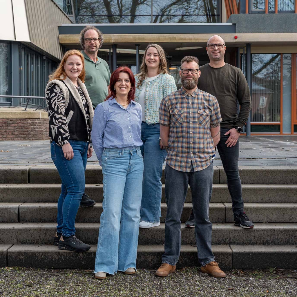 Zes medewerkers poseren op de trap voor het gemeentehuis.